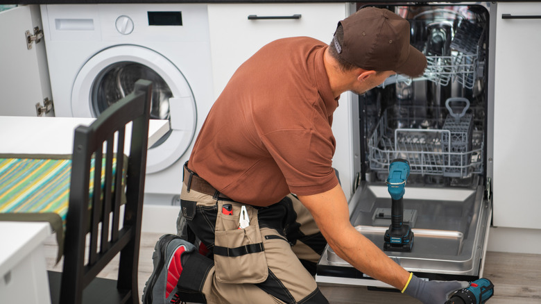 person kneeling on the floor installing a dishwasher in the kitchen alongside a washing machine
