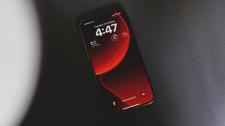 IPhone on a gray textured surface with a red and black wallpaper.