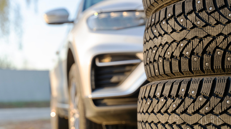 Stack of studded tires with vehicle in the background.