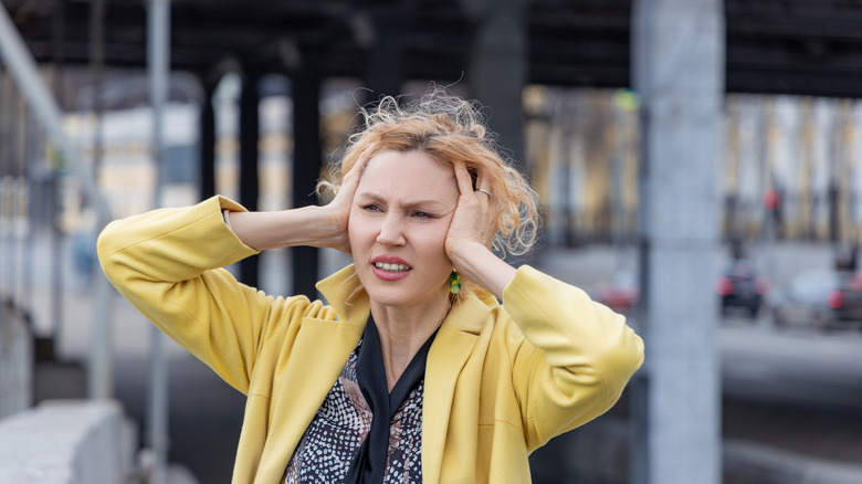 Woman standing near road with hands over ears to block out noise pollution.