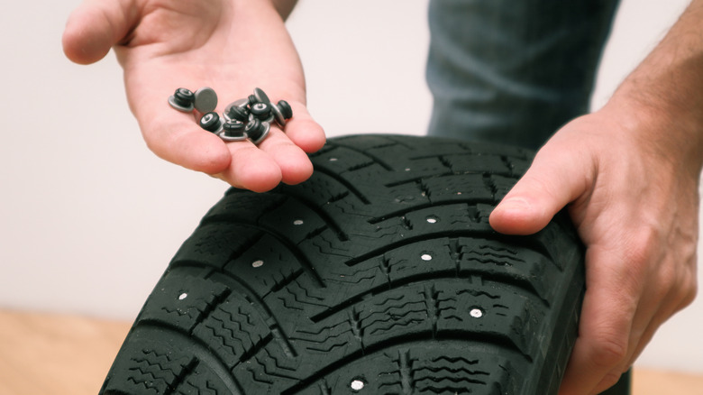 Hand holding studs in front of studded tire.