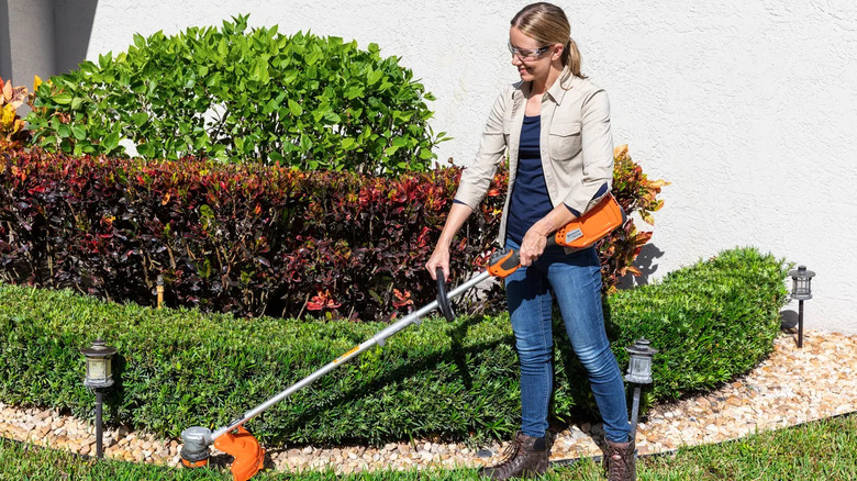 A woman using a Husqvarna Weed Eater 329iL string trimmer in a front yard