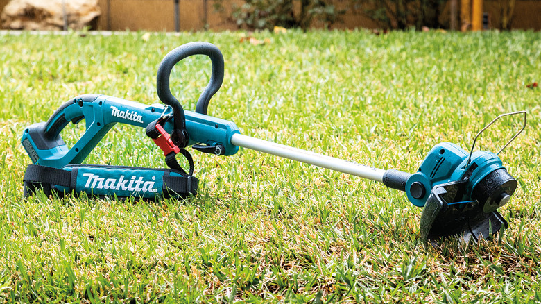 a Makita 18V LXT cordless string trimmer laying on a grass lawn