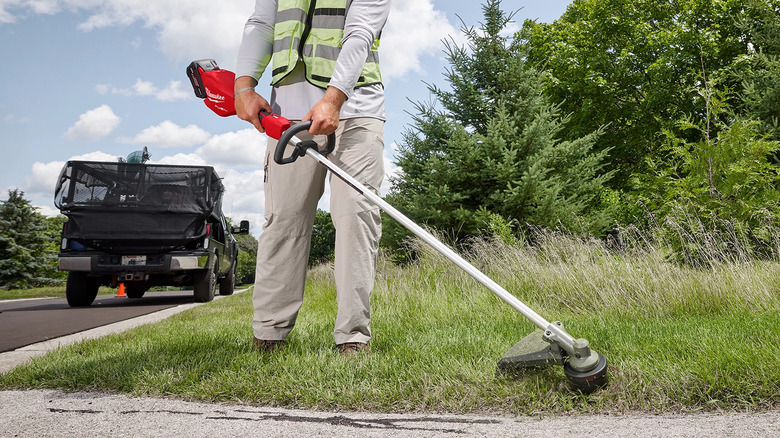 worker wearing a yellow caution vest using a Milwaukee M18 Fuel 16-inch string trimmer on grass