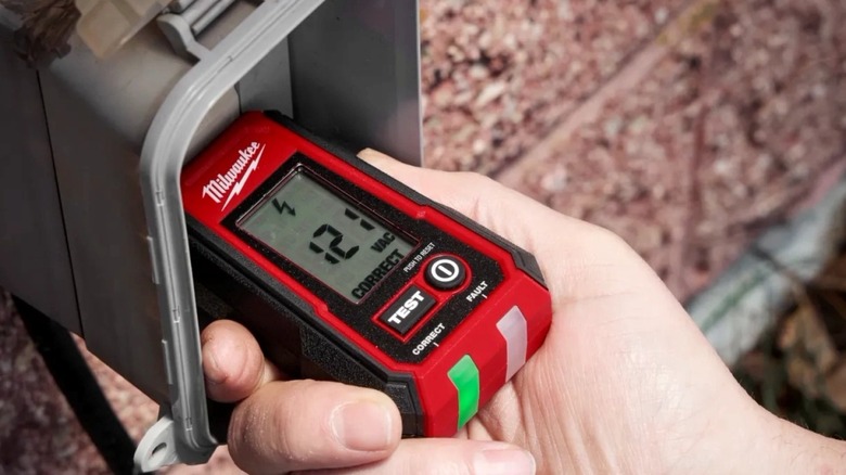 A person using the Milwaukee Tool digital GFCI receptacle tester on an outdoor outlet.