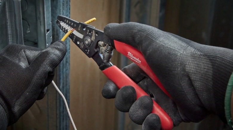 A person wearing safety gloves ising the Milwaukee Tool wire stripper to remove insulation from electrical wire.