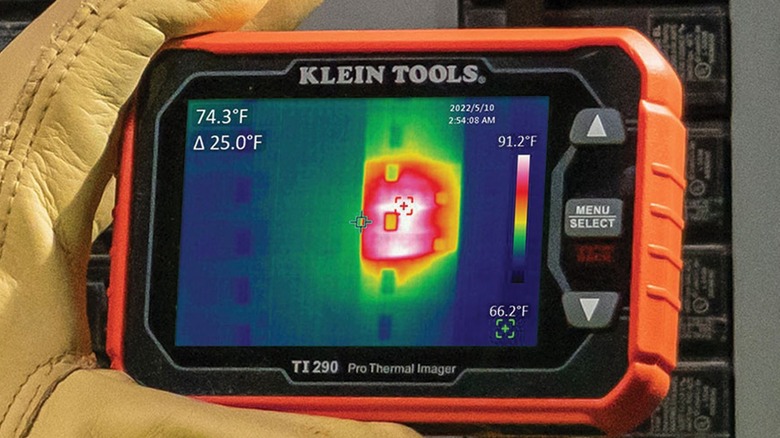 A worker wearing safety gloves using the Klein Tools pro thermal camera to check for heat generated by a circuit breaker panel.