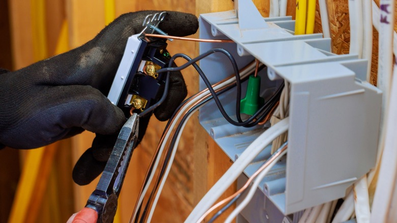 A person wearing safety gloves installing an outlet in an electrical box.