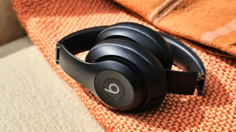 A pair of Beats headhphones laying on an orange blanket on a brown sofa