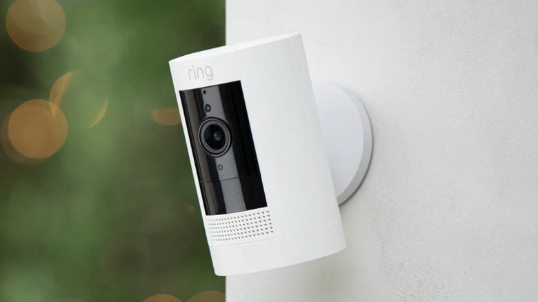 A white Ring stick-up camera mounted on a white exterior wall