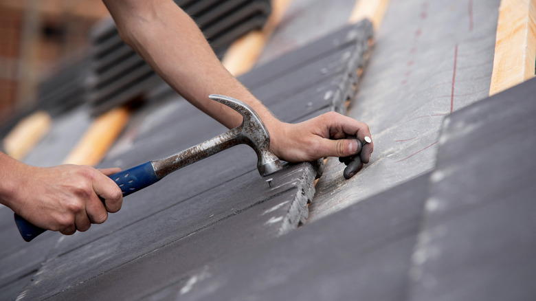 A person nailing on roof material.