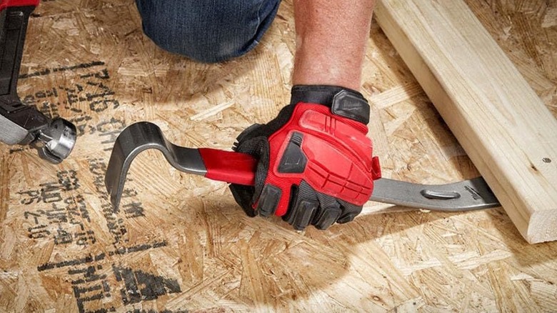 A person using a Milwaukee pry bar on wood.