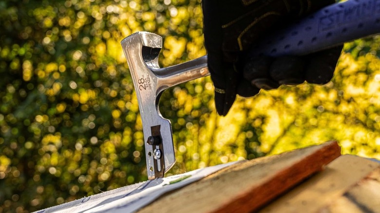 A person using a roofing hammer on shingles.