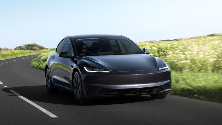 A dark gray Tesla Model 3 on a country road