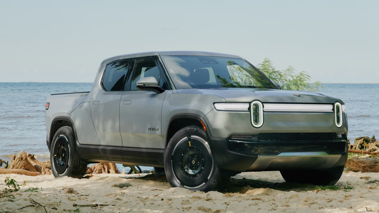 A silver Rivian R1T parked on sand near water