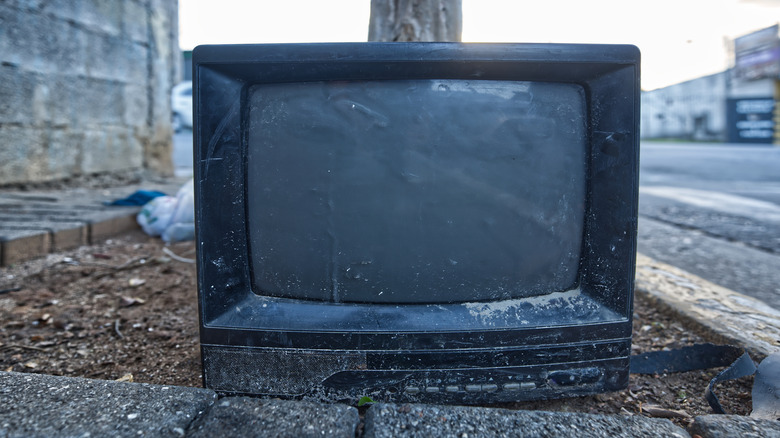 An old CRT television on dirt next to a road