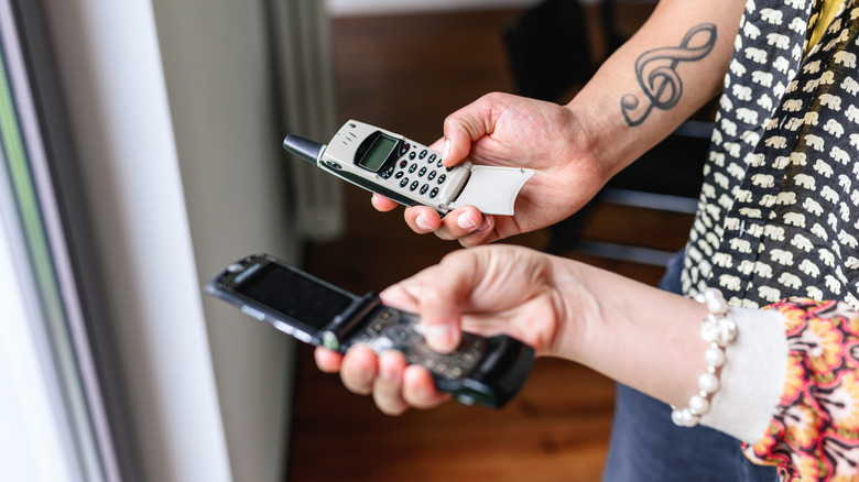 Two people holding and using old flip phones