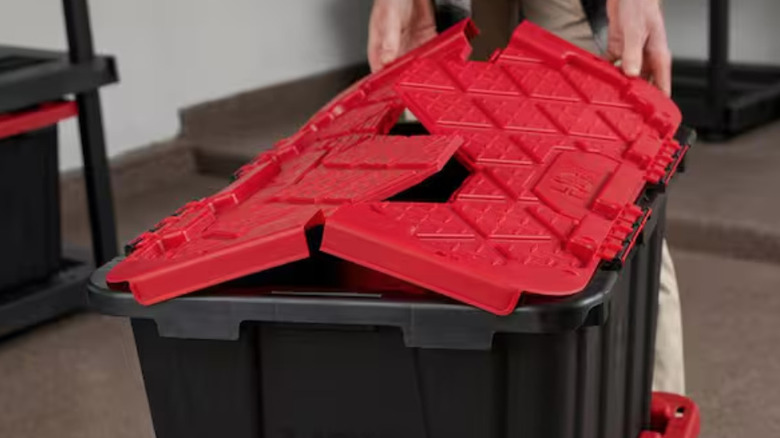 Man lifting lid on one of two HDX red-lidded flip-top totes