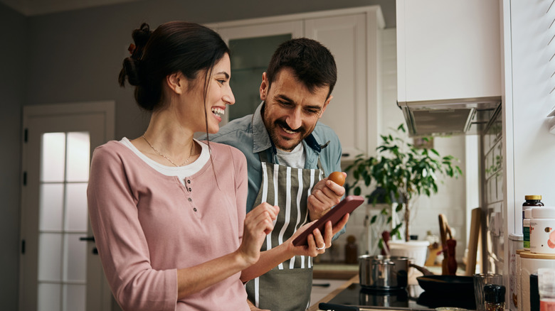 A couple using a phone while cooking