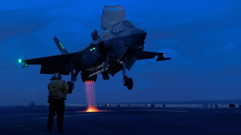 F-35B landing by the sea in the night, with flaming thrust visible under the jet