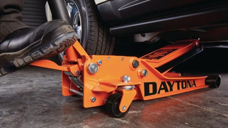 Using the foot-pump option on an orange Daytona floor jack from Harbor Freight to raise the jack under a car.