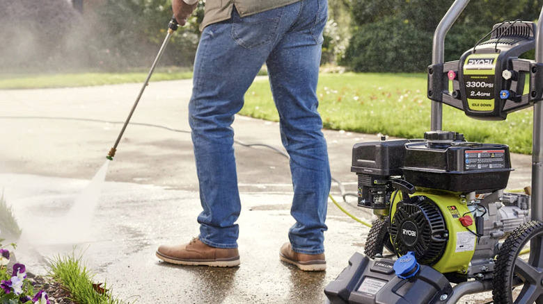 A person using a gas powered Ryobi pressure watcher