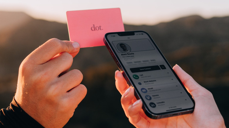 Hand holding Dot. digital business card in front of another hand holding phone.