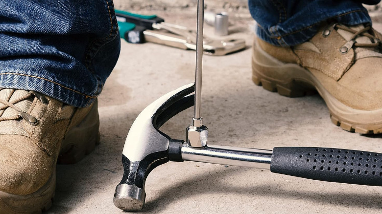 A telescoping magnetic pickup tool lifting a hammer from the ground.