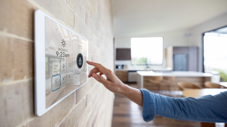 A hand touching a wall-mounted smart home hub.
