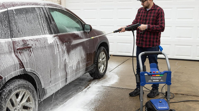 A person using a Westinghouse pressure washer to wash a car