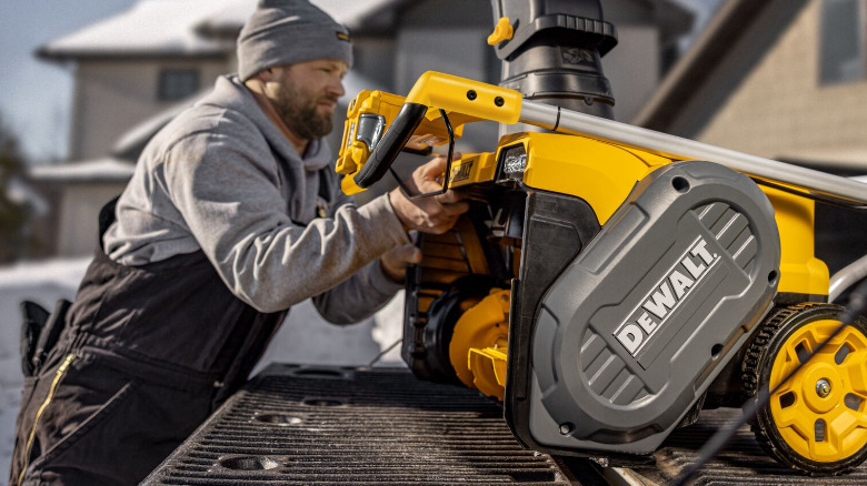 A person loading a DeWalt snow blower on a pickup truck.
