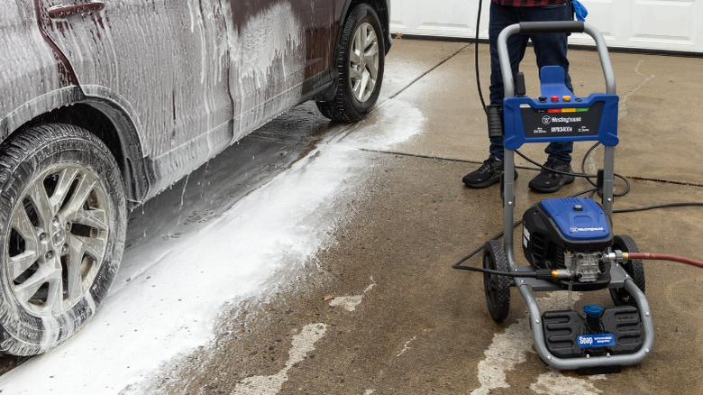 A Westinghouse pressure washer next to a car covered in soap.