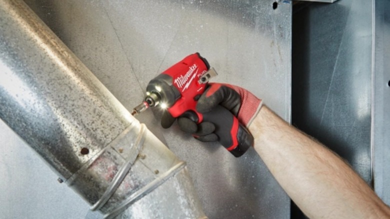 A person using a Milwaukee impact driver on metal.