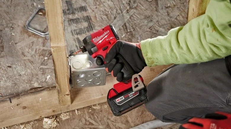 A person using a Milwaukee impact driver on wood.