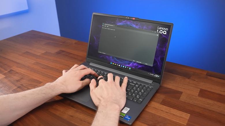A person using the Lenovo LOQ Essential on a wooden table, blue wall in the background