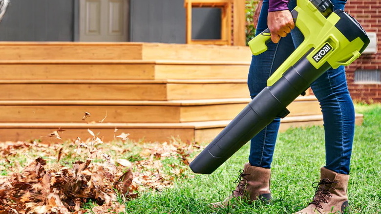 woman using Ryobi 18V ONE+ 350 CFM leaf blower on leaves in backyard