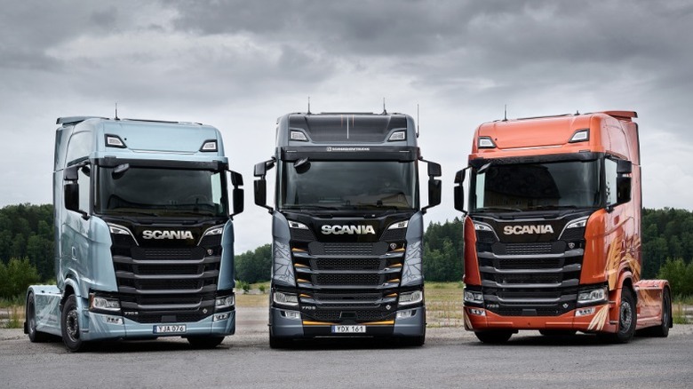 Three special edition Scania S-series trucks parked under a cloudy sky