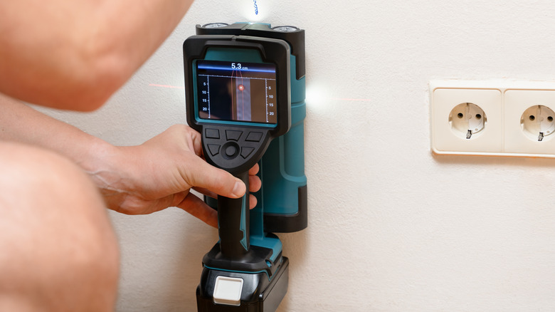 A person using a blue Makita multi-surface scanner on a white wall
