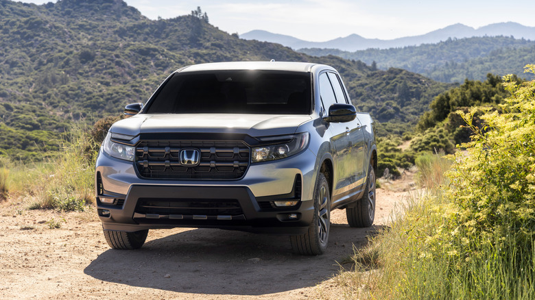 A silver 2026 Honda Ridgeline on a dirt trail, mountains in the background