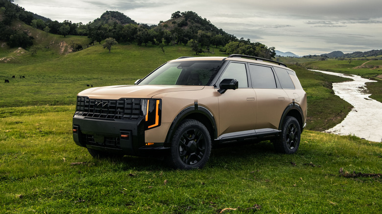 A brown 2027 Kia Telluride parked on grass near hills and a river