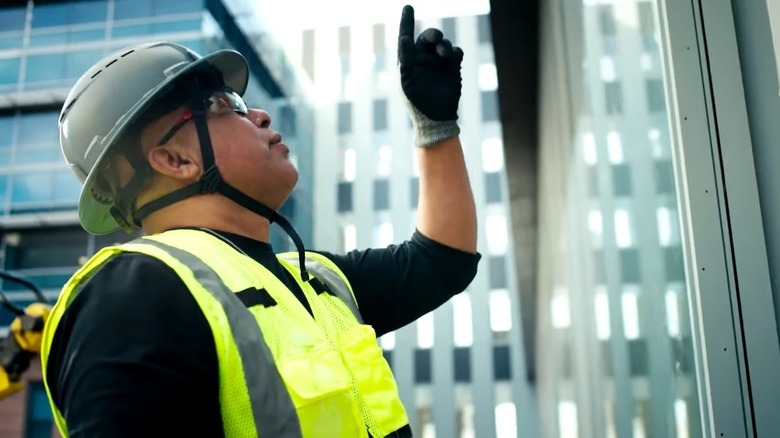 Person wearing safety helmet gestures upwards.