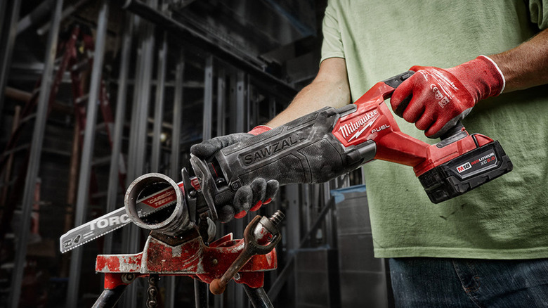 A person cutting a metal pipe with a Milwaukee Sawzall.
