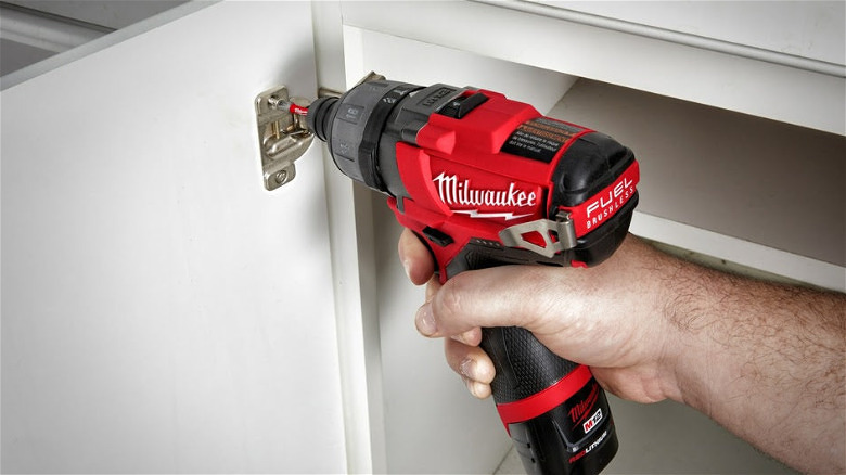 Using the M12 Fuel Cordless Screwdriver to drive a screw into a cabinet door hinge assembly.