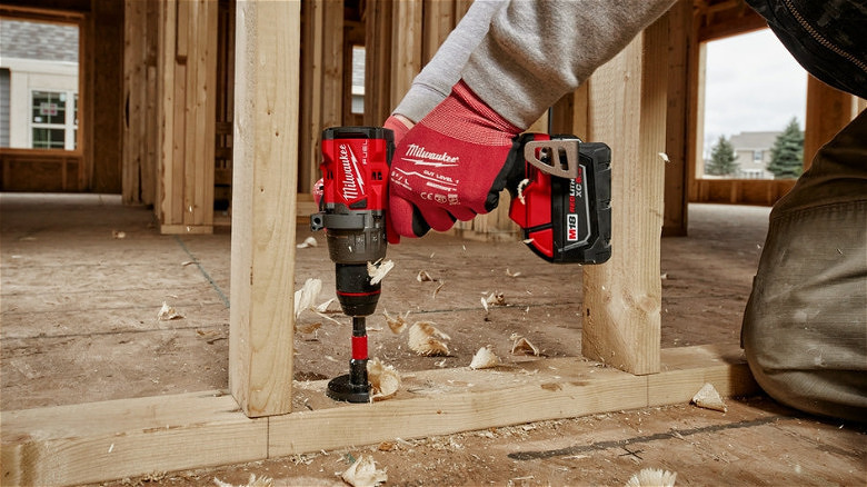 A worker using a Milwaukee Hammer Drill/Driver to drill a hole in a wooden joist.