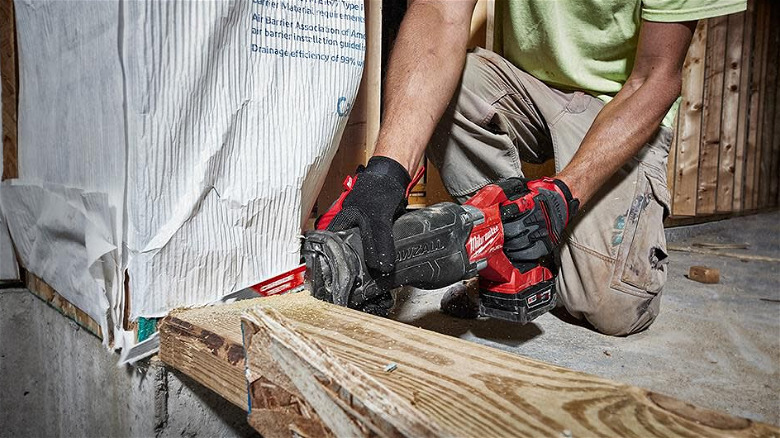 A worker uses the Milwukee Sawzall to cut through a wooden floor beam.