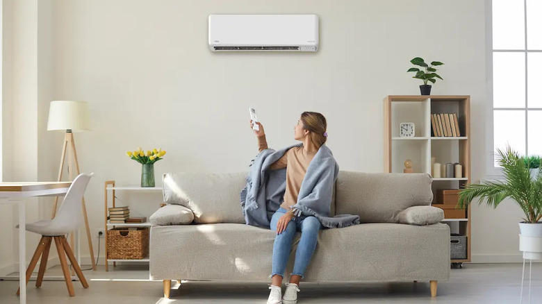 a woman sitting on a couch and using a remote to adjust the temperature of a Fujitsu air conditioner on the wall