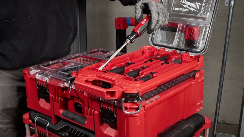 A person holding a Milwaukee screwdriver over a tool box.