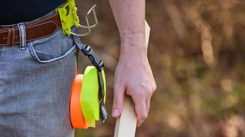 The Ryobi Strap Hook with rolls of tapes attached,  hanged on a person's belt.