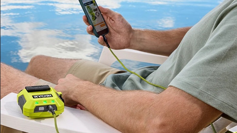 A man sitting poolside charging his phone with the Ryobi USB Lithium 3-port charger and power source.