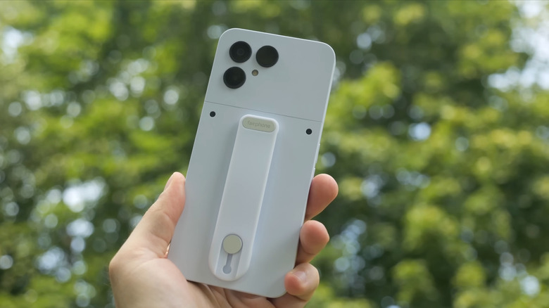 A person holding up a white Fairphone 6, trees in the background